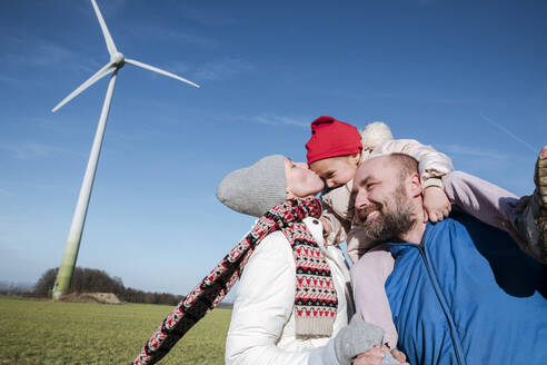 Happy parents with little daughter against sky with wind wheel in the background - VYF00067