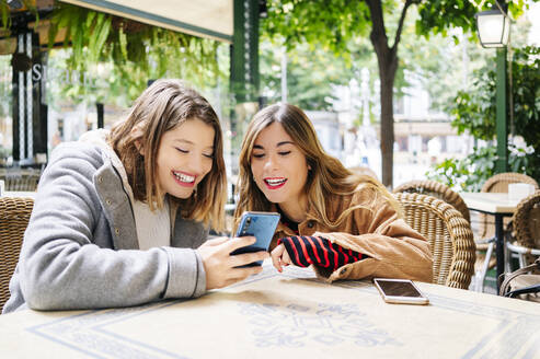 Zwei glückliche junge Frauen mit Smartphone in einem Straßencafé - DGOF00556