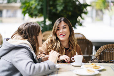 Zwei glückliche junge Frauen unterhalten sich in einem Straßencafé - DGOF00560