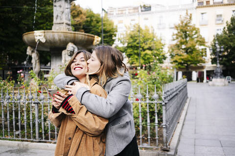 Zwei glückliche junge Frauen umarmen sich in der Stadt, lizenzfreies Stockfoto