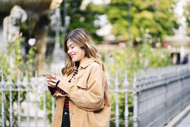 Smiling young woman using smartphone in the city - DGOF00565