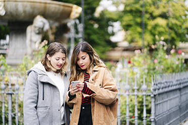 Zwei junge Frauen benutzen ein Smartphone in der Stadt - DGOF00567