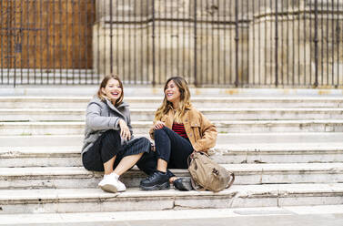 Two happy young women sitting on stairs in the city - DGOF00570