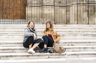 Zwei glückliche junge Frauen sitzen auf einer Treppe in der Stadt - DGOF00570