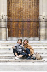 Zwei glückliche junge Frauen sitzen auf einer Treppe in der Stadt und machen ein Selfie - DGOF00572