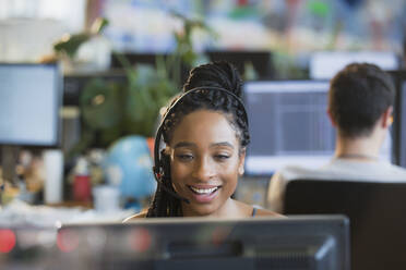 Lächelnde Geschäftsfrau mit Headset bei der Arbeit am Computer im Büro - HOXF05814