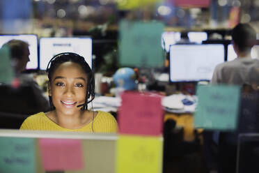 Porträt einer selbstbewussten, lächelnden Geschäftsfrau mit Headset, die am Computer hinter Haftnotizen im Büro arbeitet - HOXF05826