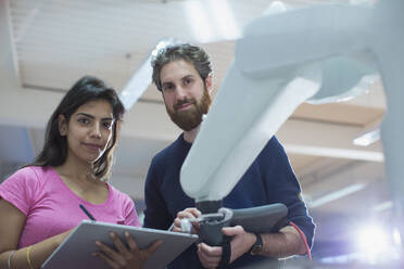 Portrait confident engineers with digital tablet programming robotic arm in office - HOXF05830