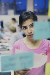 Focused businesswoman planning, looking at adhesive notes in office - HOXF05839