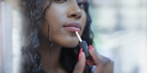 Close up beautiful young woman applying lip gloss - HOXF05845