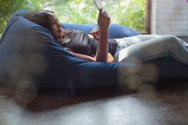 Young woman relaxing using digital tablet in beanbag chair - HOXF05856