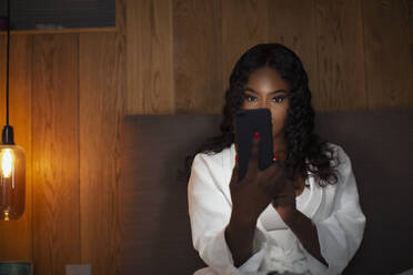 Young woman using smart phone in dark bedroom - HOXF05884