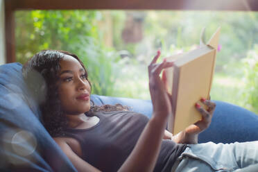 Young woman relaxing reading book in beanbag chair - HOXF05890