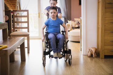 Junge schiebt seinen Bruder mit Down-Syndrom im Rollstuhl - HOXF05898