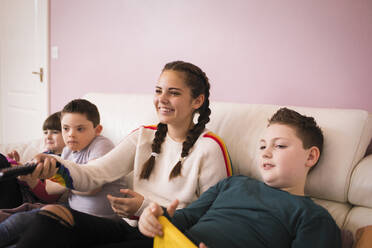 Glückliches Mädchen sieht mit Geschwistern auf dem Sofa fern - HOXF05905
