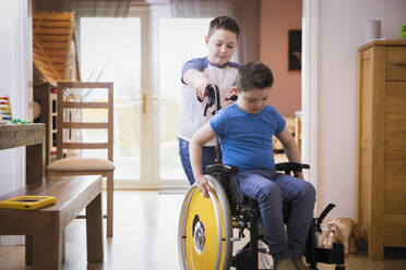 Junge schiebt seinen Bruder mit Down-Syndrom im Rollstuhl - HOXF05957