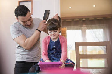 Vater bürstet die Haare seiner Tochter mit einem digitalen Tablet - HOXF05958