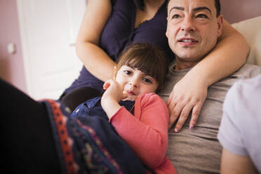 Happy girl cuddling with father on sofa - HOXF05963