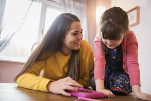 Fröhliche Schwestern mit digitalem Tablet am Tisch - HOXF05976