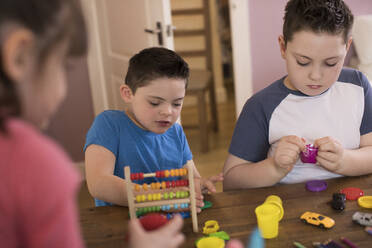 Junge mit Down-Syndrom und Bruder spielen mit Spielzeug am Tisch - HOXF05984
