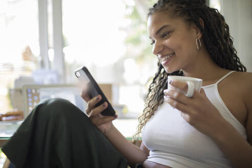 Junge Frau trinkt Kaffee und benutzt ein Smartphone - HOXF05990