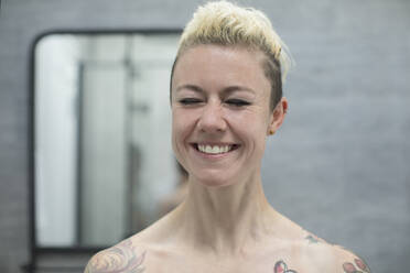 Porträt glückliche sorglose Frau mit Tattoos lachend im Badezimmer - HOXF06024
