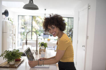 Portrait happy young female freelancer working at laptop in kitchen - HOXF06042