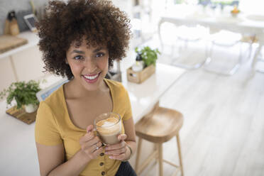 Porträt glückliche junge Frau trinkt Cappuccino in Küche - HOXF06068