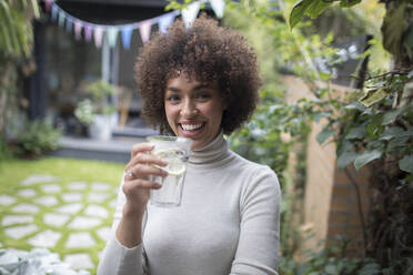 Porträt einer glücklichen jungen Frau, die auf einer Terrasse Wasser trinkt - HOXF06071