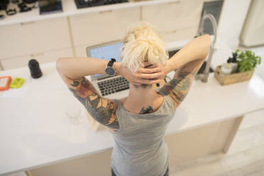 Junge Freiberuflerin mit Tattoos arbeitet am Laptop in der Küche - HOXF06108
