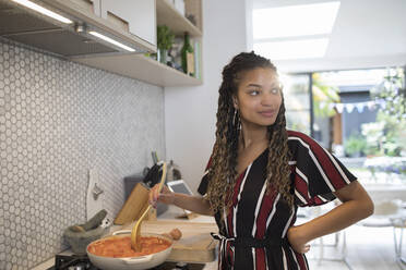 Young woman cooking at stove in kitchen - HOXF06113