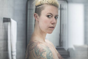 Portrait confident woman with tattoos and bare shoulders in bathroom - HOXF06121