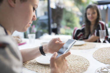 Young woman using smart phone at dining table - HOXF06129