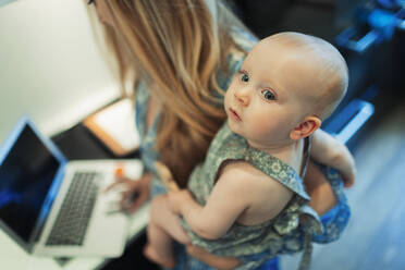 Mother working at laptop and holding cute baby daughter - HOXF06133