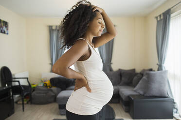 Müde junge schwangere Frau im Wohnzimmer - HOXF06148