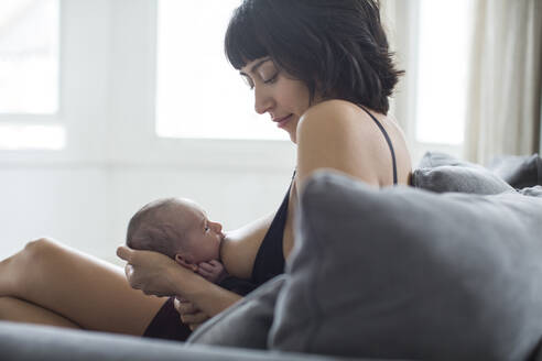 Mutter, die ihr neugeborenes Baby auf dem Sofa stillt - HOXF06179