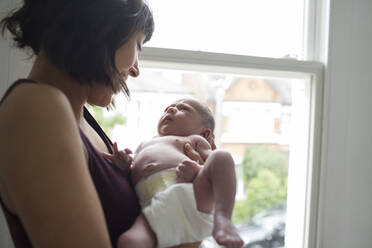 Mother holding cute newborn baby boy at window - HOXF06182