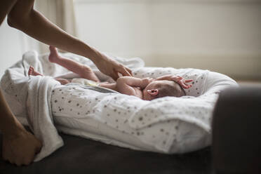 Mother reaching for newborn baby son in bassinet - HOXF06204