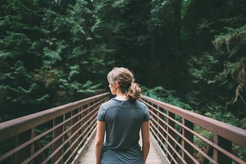 Rückansicht von Mid Adult Frau zu Fuß auf dem Steg im Wald, lizenzfreies Stockfoto