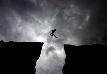 Silhouette Man Jumping Over Cliffs Against Cloudy Sky - EYF01673