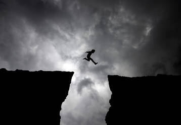 Silhouette Mann springt über Klippen gegen bewölkten Himmel - EYF01673