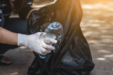 Midsection Of Woman Picking Crushed Plastic Bottle From Road - EYF01749