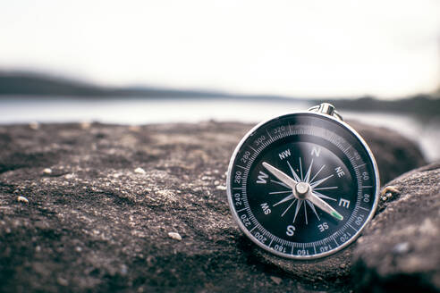 Close-Up Of Navigational Compass On Stone Wall By Lake - EYF01773