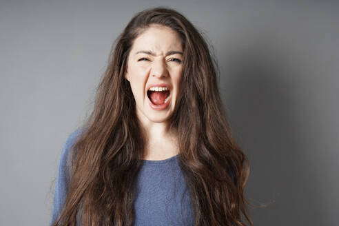 Porträt einer schreienden jungen Frau vor grauem Hintergrund - EYF01779