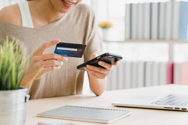 Midsection Of Woman Holding Credit Card While Using Mobile Phone For Online Shopping On Table - EYF01794