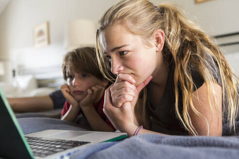 13 Jahre alte Schwester und ihr Bruder schauen auf dem Bett auf den Laptop - MINF14272