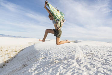 A teenage girl leaping in the air, in a wide open space, sand dunes. - MINF14294