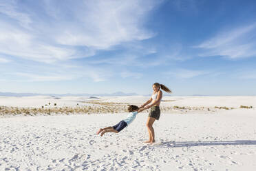 A teenage girl swinging her 6 year old brother in sand, - MINF14303