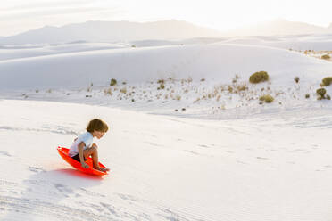 A young boy sledding down white sand dunes - MINF14313