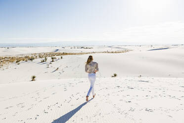 A teenage girl standing looking at a vast open space of sand dunes. - MINF14320